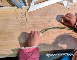 Threading a pipecleaner through pieces of wood for a handcrafted wooden toy alligator